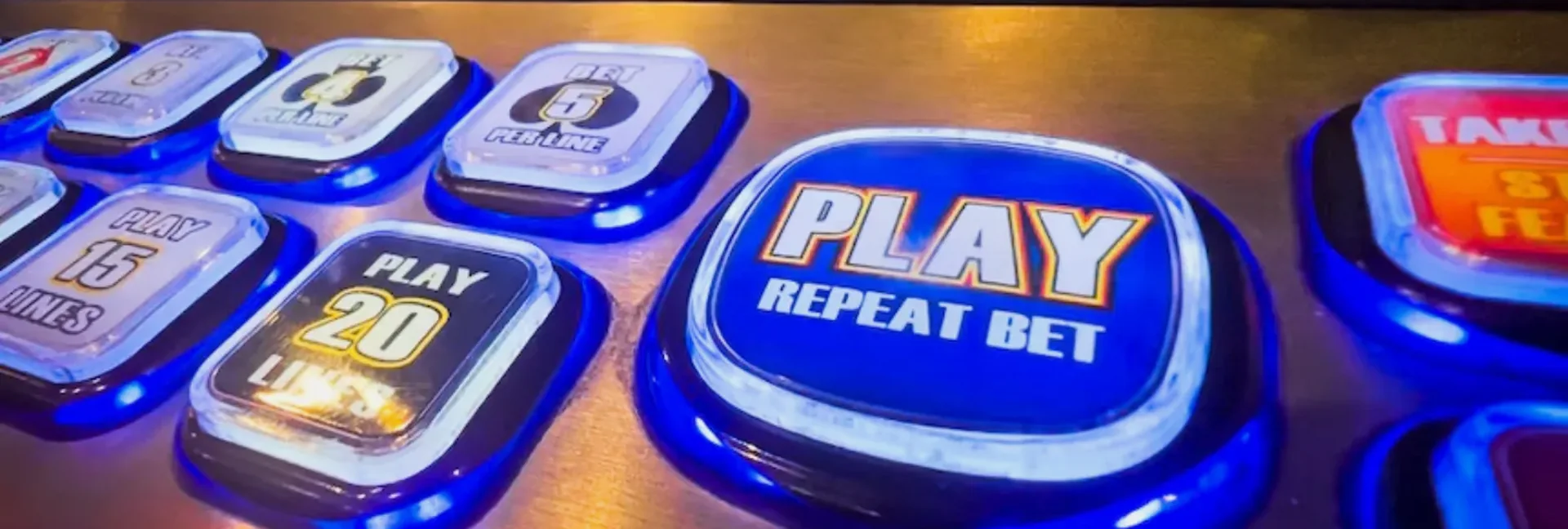 Close-up of a gaming machine button deck lit in blue over brushed steel